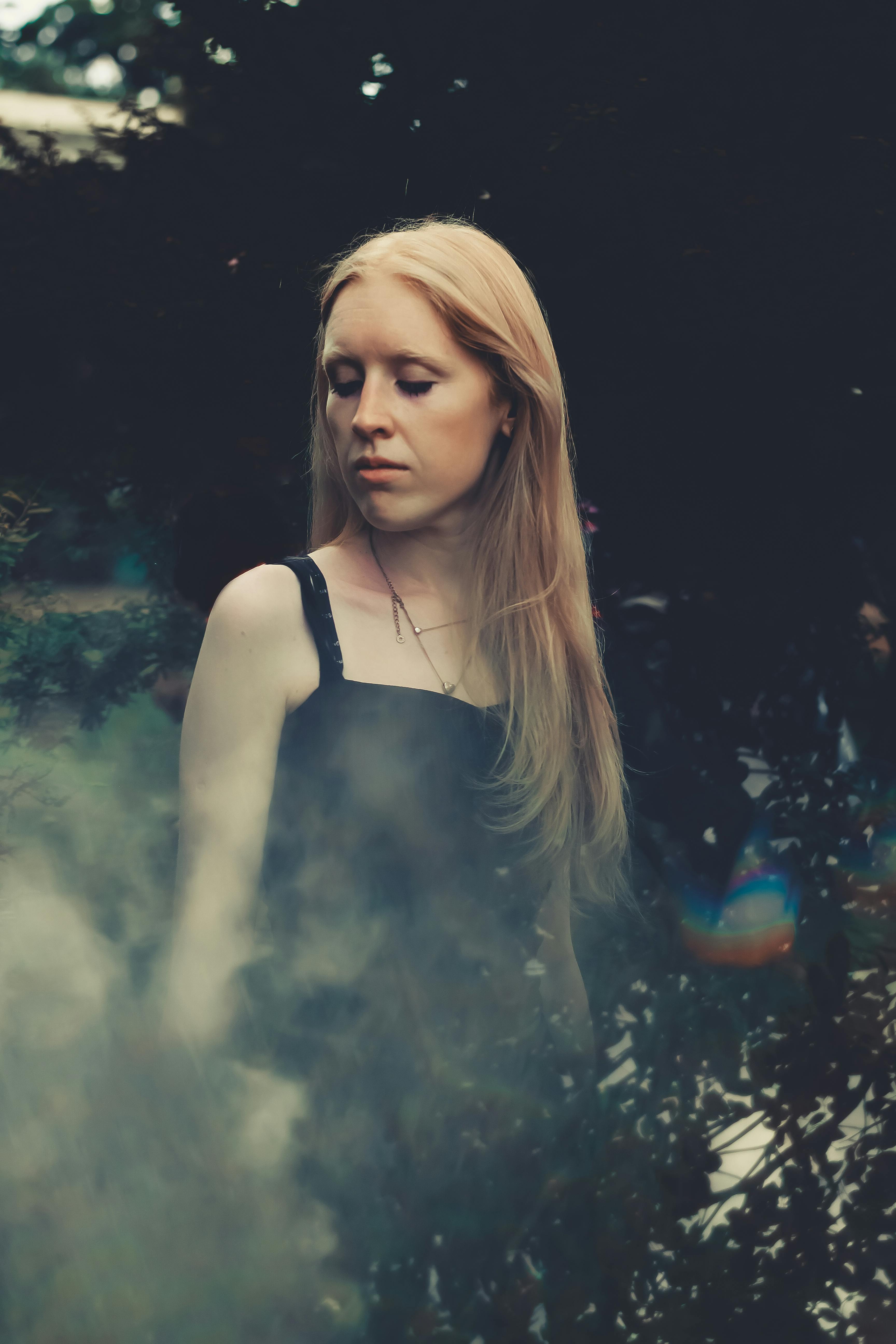 一位金发年轻女子身处薄雾与绿叶环绕的大自然中，肖像宁静安详