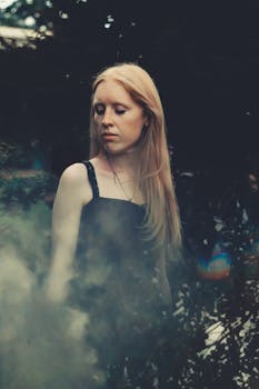 一位金发年轻女子身处薄雾与绿叶环绕的大自然中，肖像宁静安详