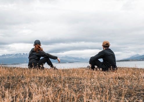 Couple sitting on grass, admiring a lake in Ushuaia, Argentina.