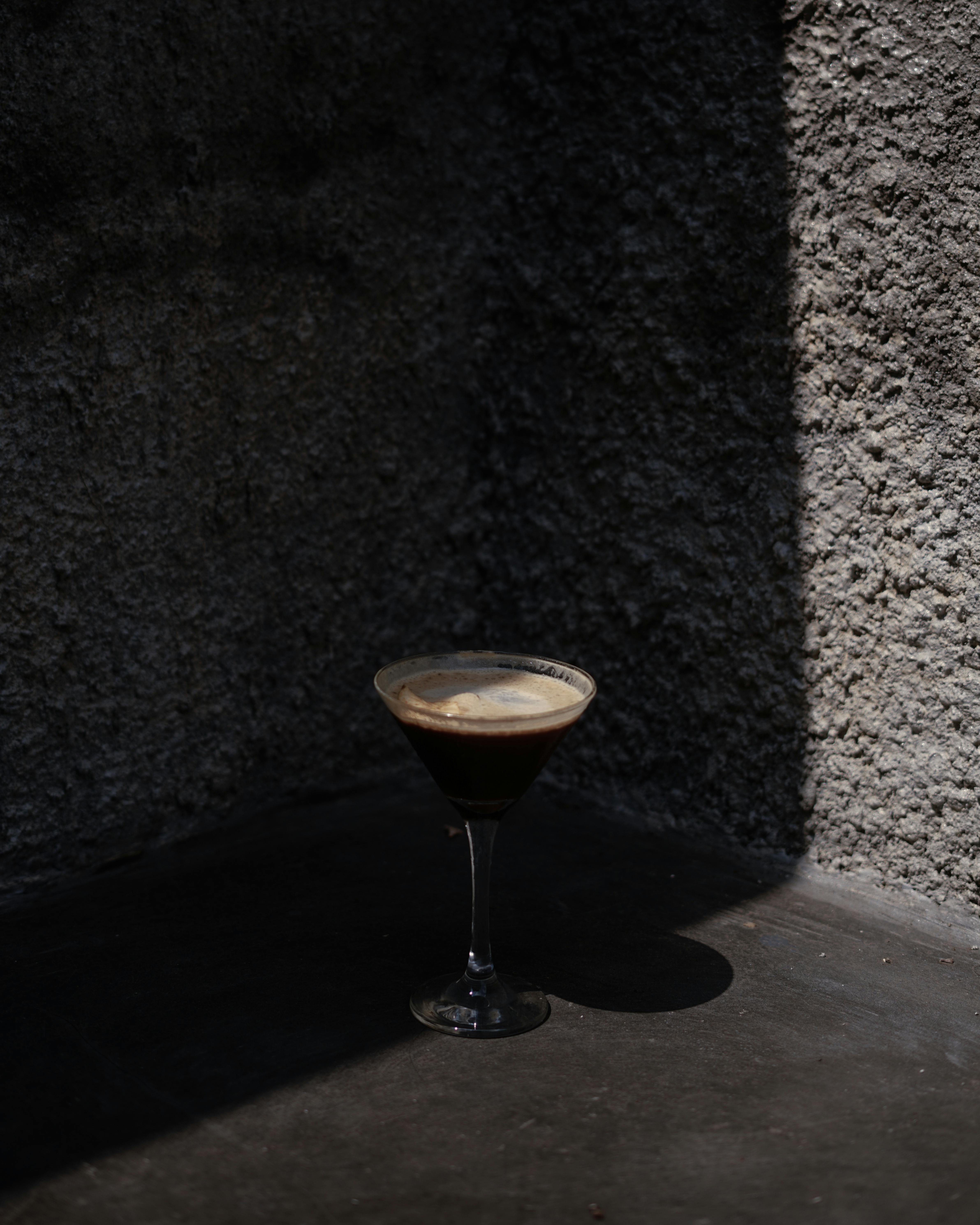 A martini glass filled with a dark beverage casting a shadow on a textured surface.