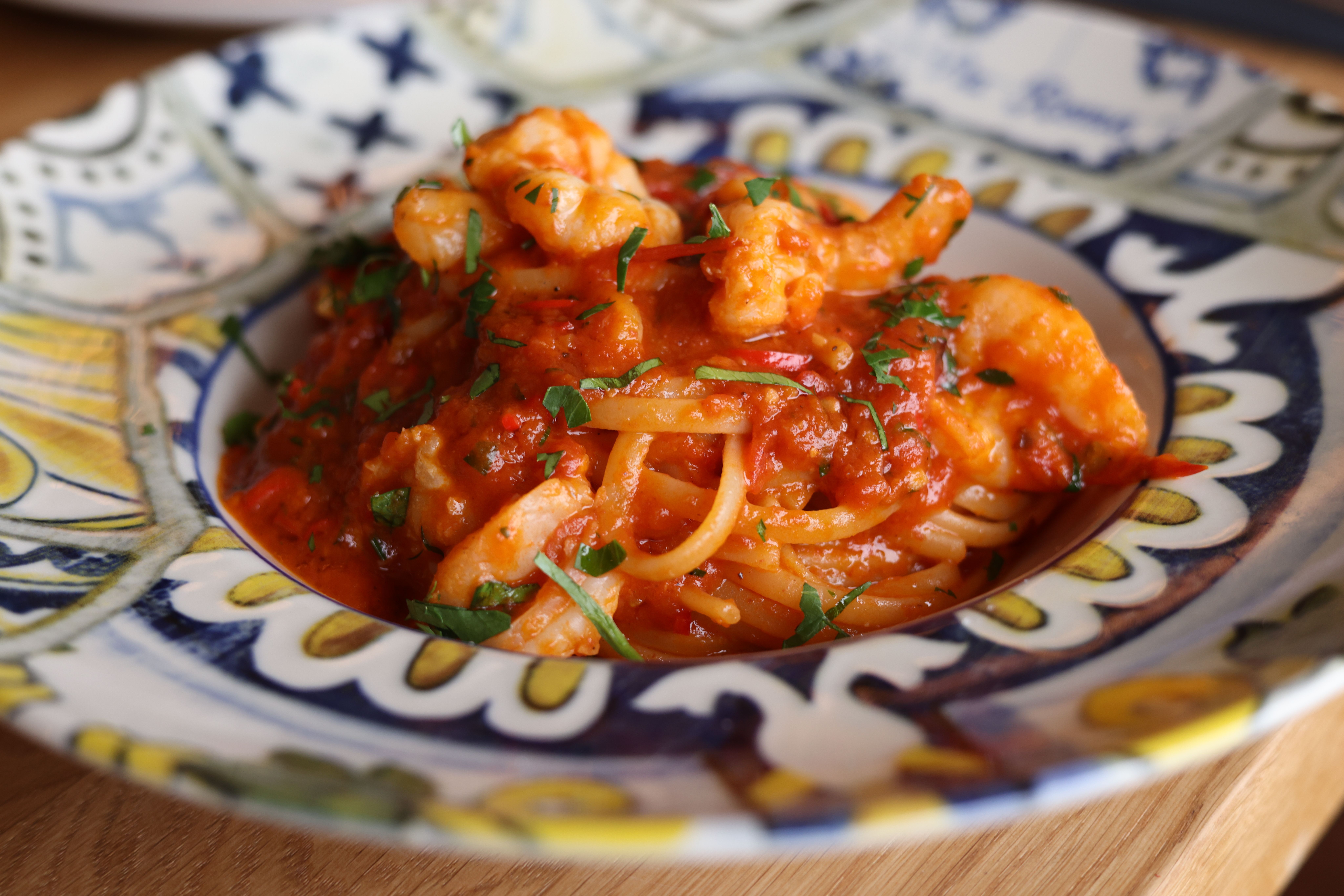 Mouthwatering shrimp pasta in rich tomato sauce garnished with herbs, served in a decorative bowl.