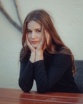 A thoughtful portrait of a woman with long brown hair sitting at a table.