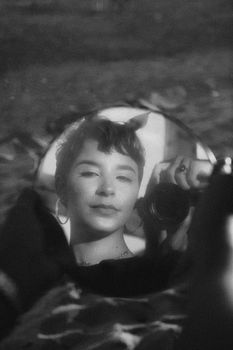 Black and white portrait of a woman taking a selfie with a mirror reflection for a creative effect.