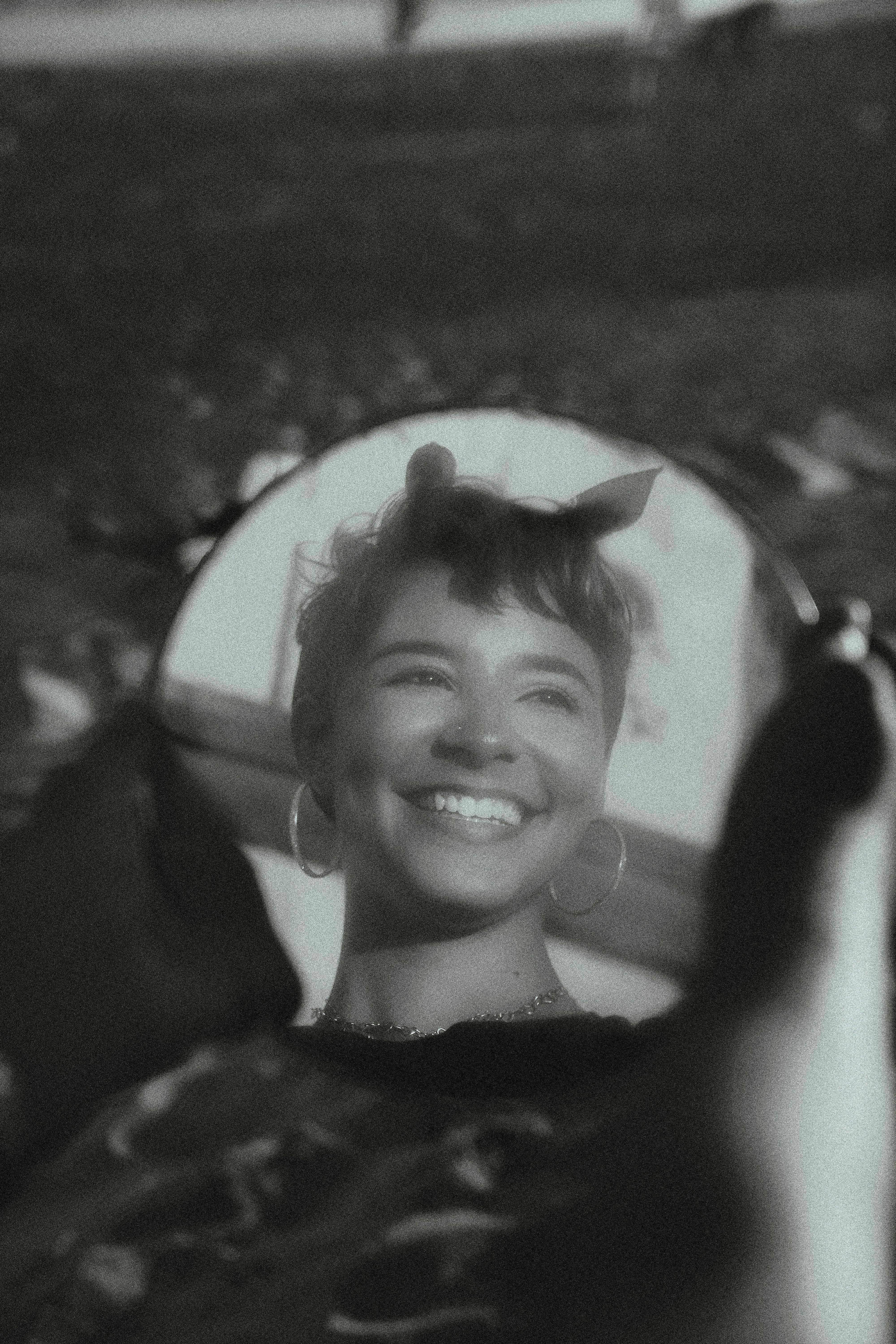 A smiling woman reflects in a handheld mirror, creating a vintage feel.