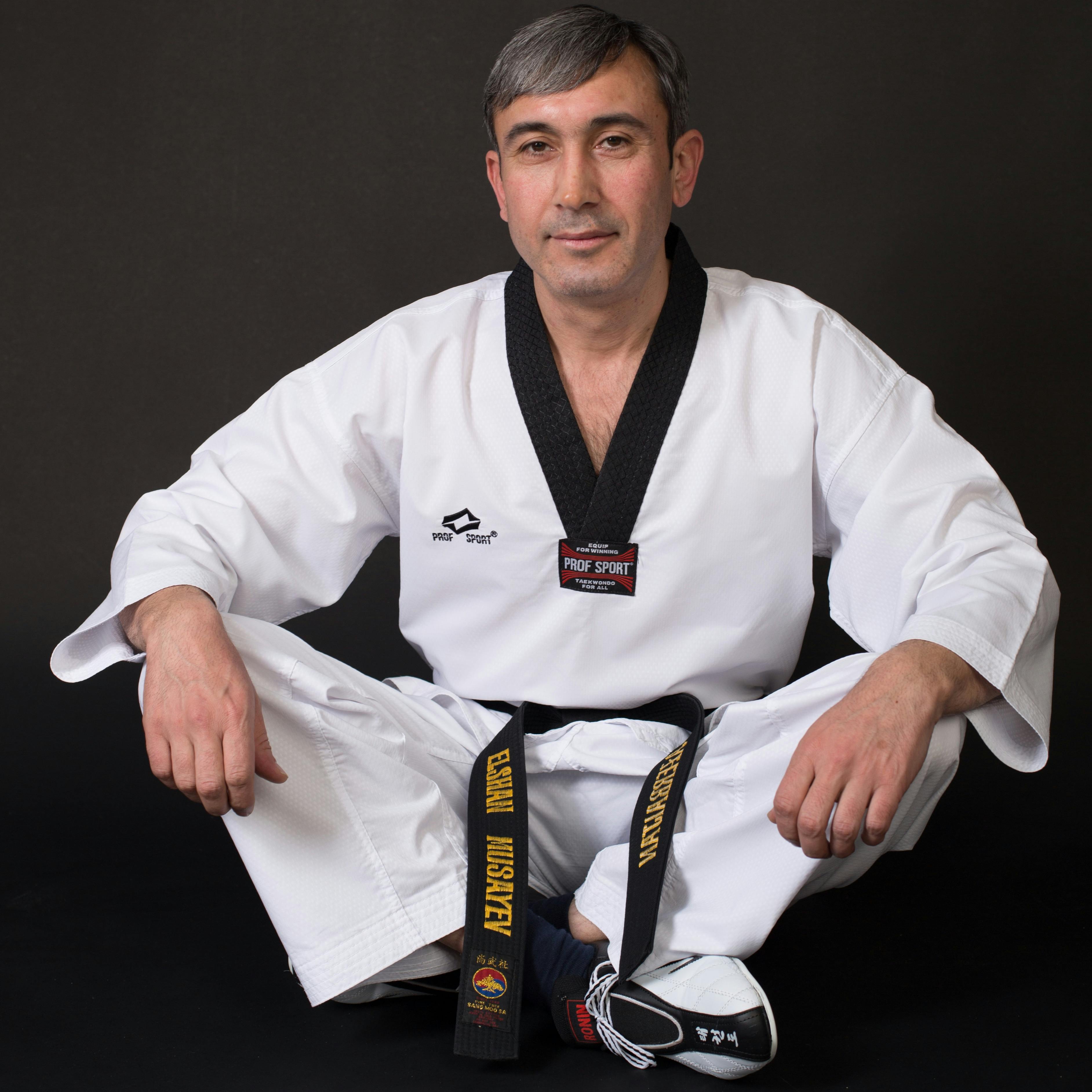 Martial artist in karate uniform with black belt sitting in studio setting.