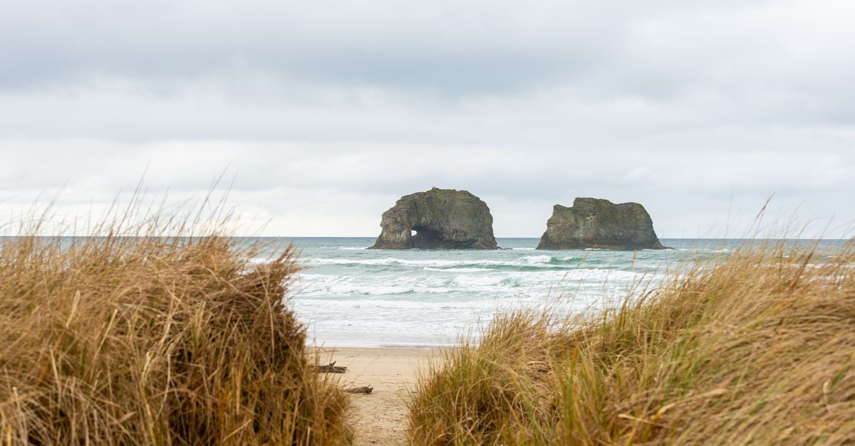 A tranquil beach scene featuring iconic sea stacks and grassy dunes under a cloudy sky.