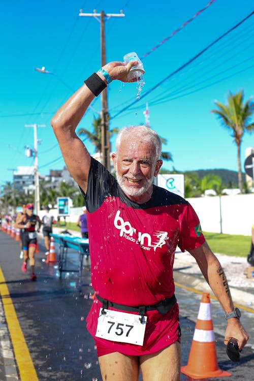 An older man running in a marathon with his hands up
