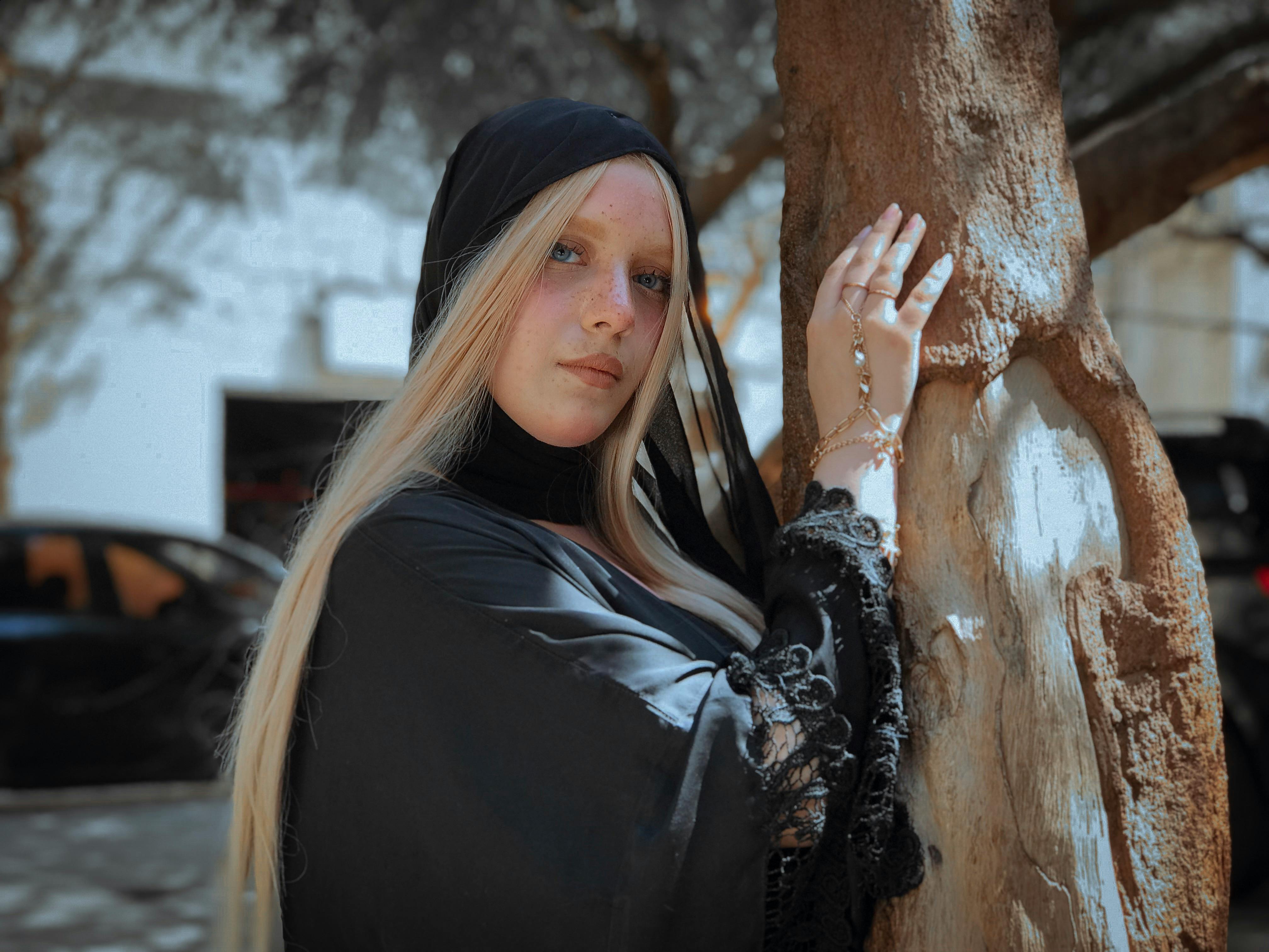 一名身着优雅黑色服装的女子在户外的一棵树旁自信而时尚地摆着姿势