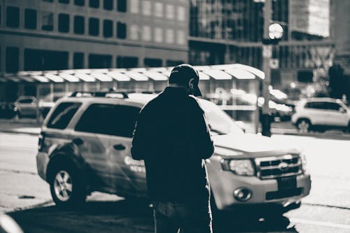 Фотография человека, стоящего возле внедорожника в дневное время в оттенках серого