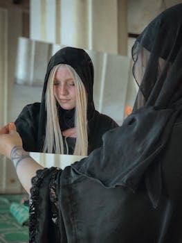 一名戴着黑色兜帽、留着金色长发的女子凝视着镜中的自己