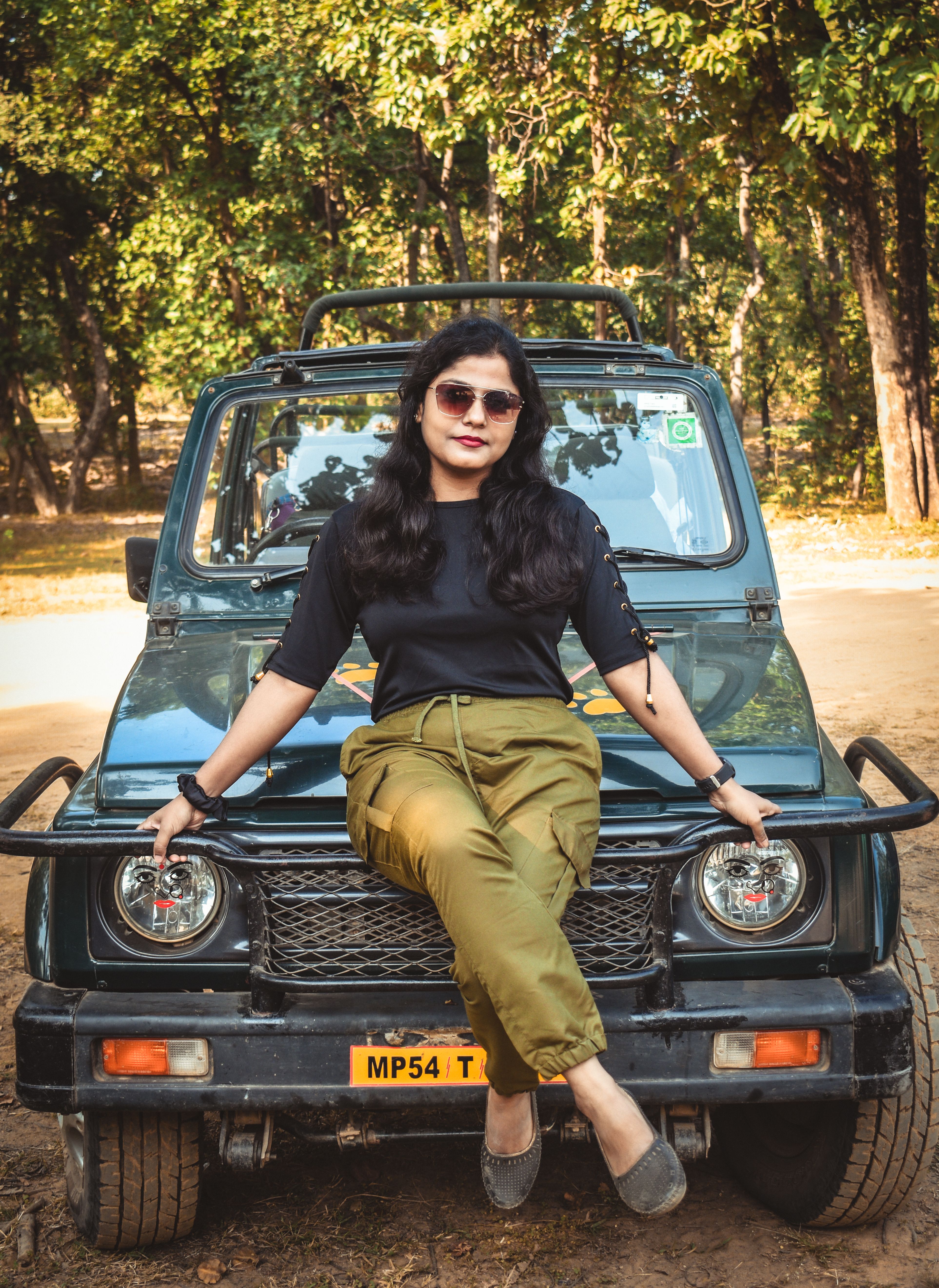 A fashionable woman in sunglasses poses confidently on an off-road vehicle in a forest setting.