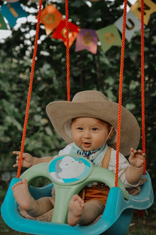 A baby in a cowboy hat sitting on a swing
