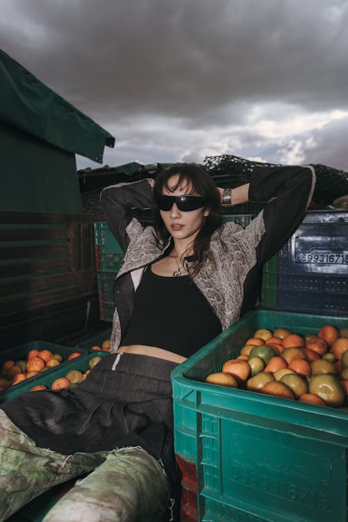 A woman sitting in a green crate with oranges