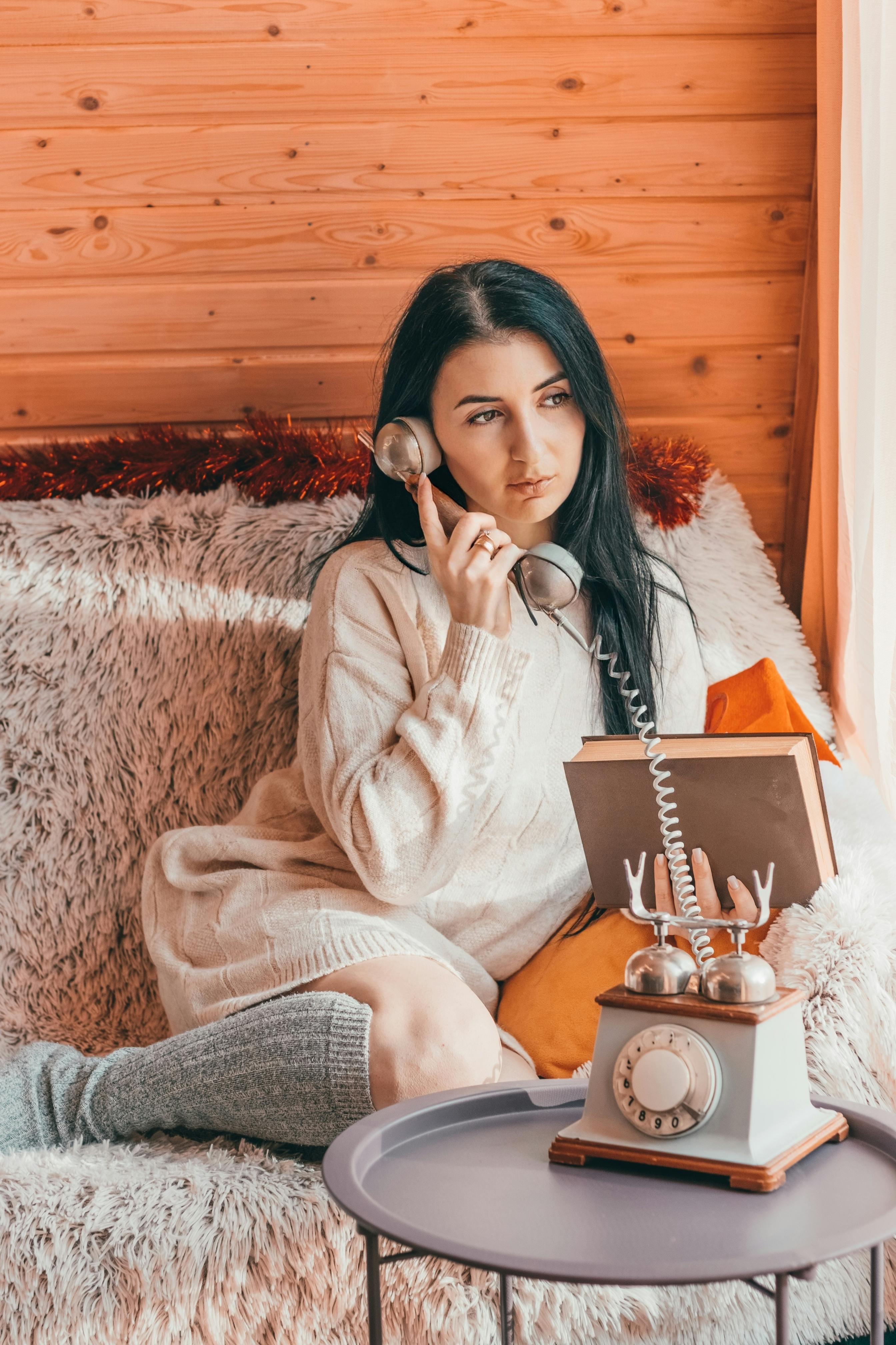 Gratis Brunette I Genser Posering Med Telefon Og Bok Arkivbilde