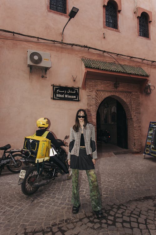 A woman standing in front of a building with a motorcycle