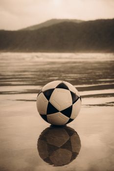 A soccer ball on the wet sands of Guarujá beach, Brazil, during sunset. Scenic reflections.
