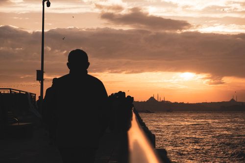 Free A man walks along the waterfront with Istanbul skyline at sunset, capturing a serene moment. Stock Photo