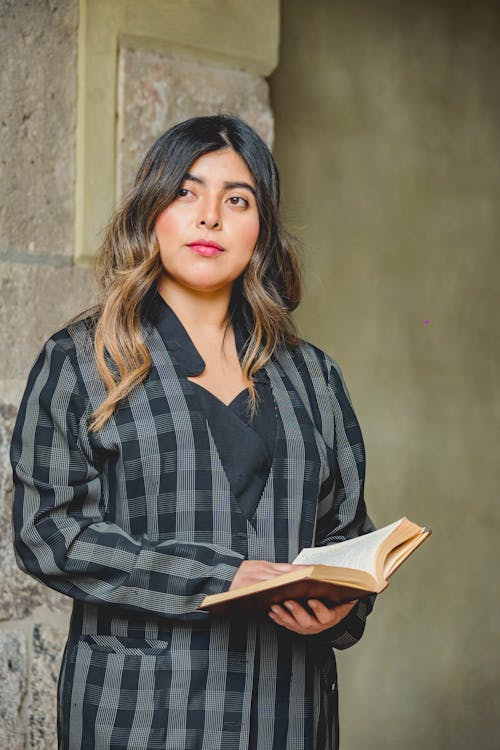 A woman in a black and white checkered dress holding a book