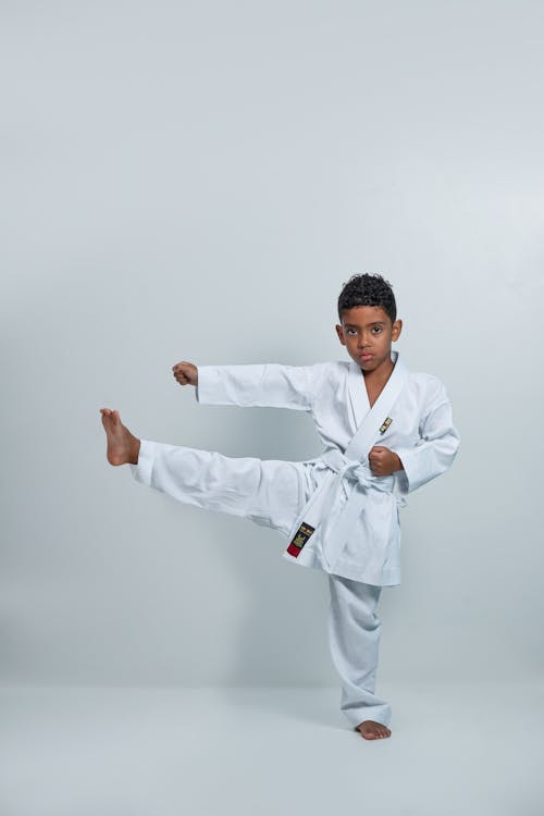A young boy in white karate outfit doing a kick