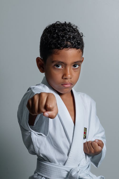 A young boy in a karate uniform pointing at the camera
