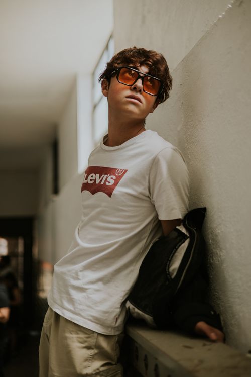 Free Fashionable young man wearing sunglasses and casual outfit, posing against a wall in a modern setting. Stock Photo