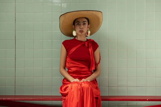 A woman in a red dress and hat sits on a bench