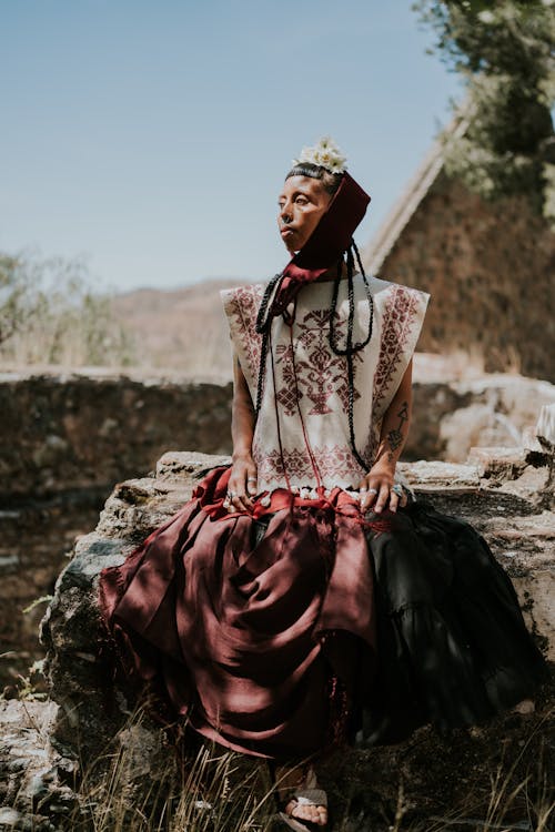 A woman in a traditional dress sitting on a rock