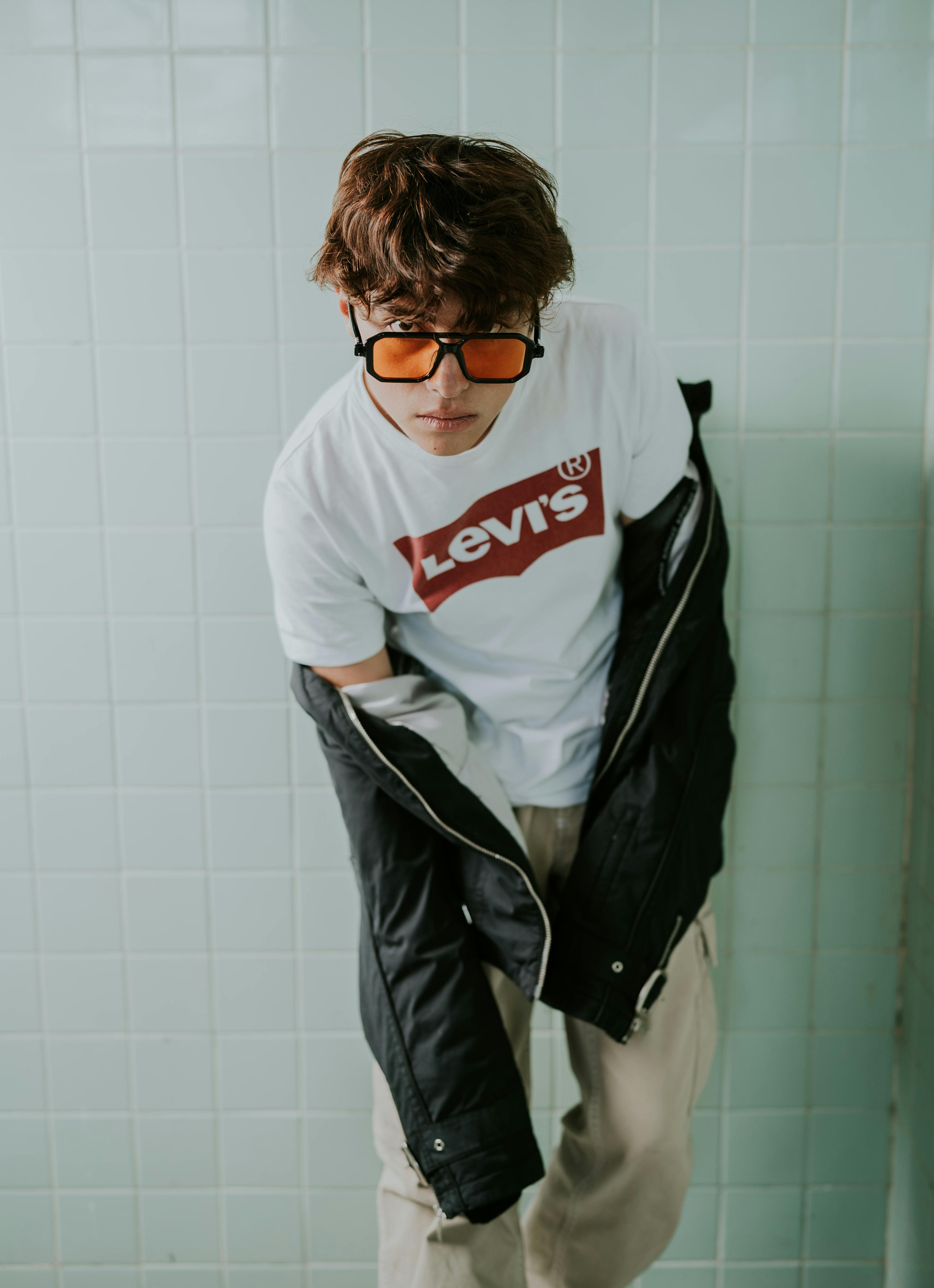 Trendy young man in sunglasses and jacket posing indoors.