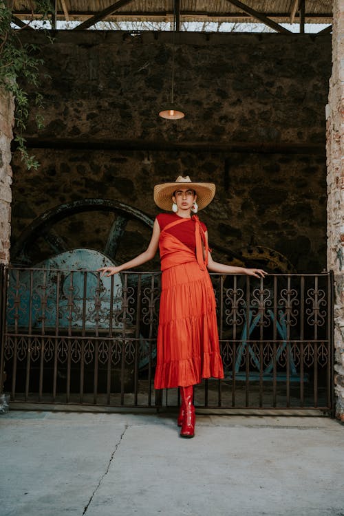 A woman in a red dress and hat standing in front of a gate