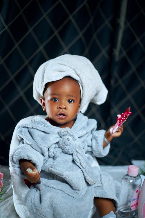A baby in a towel holding a toothbrush
