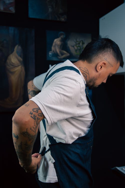A man with tattoos on his back is standing in front of paintings
