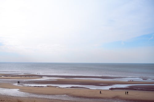 A beach with people walking on it and a sky