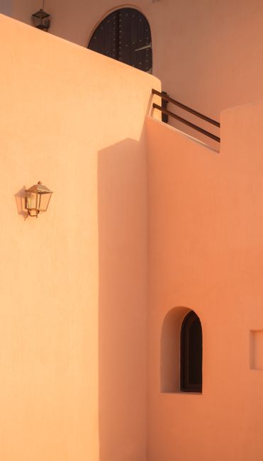 A serene pink building facade with sunlight casting artistic shadows.