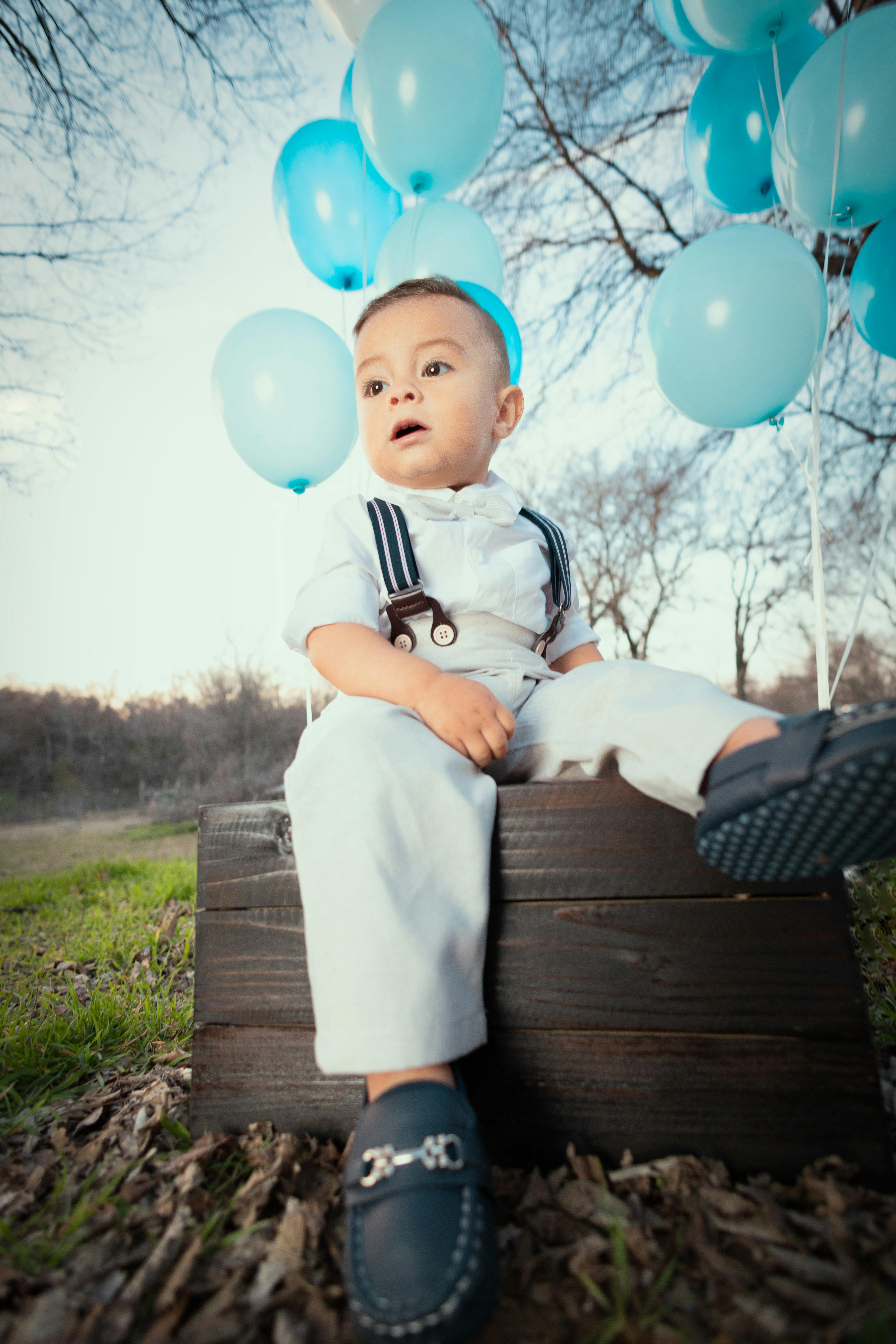 A Little Boy Sitting Outside with Blue Balloons · Free Stock Photo(00)