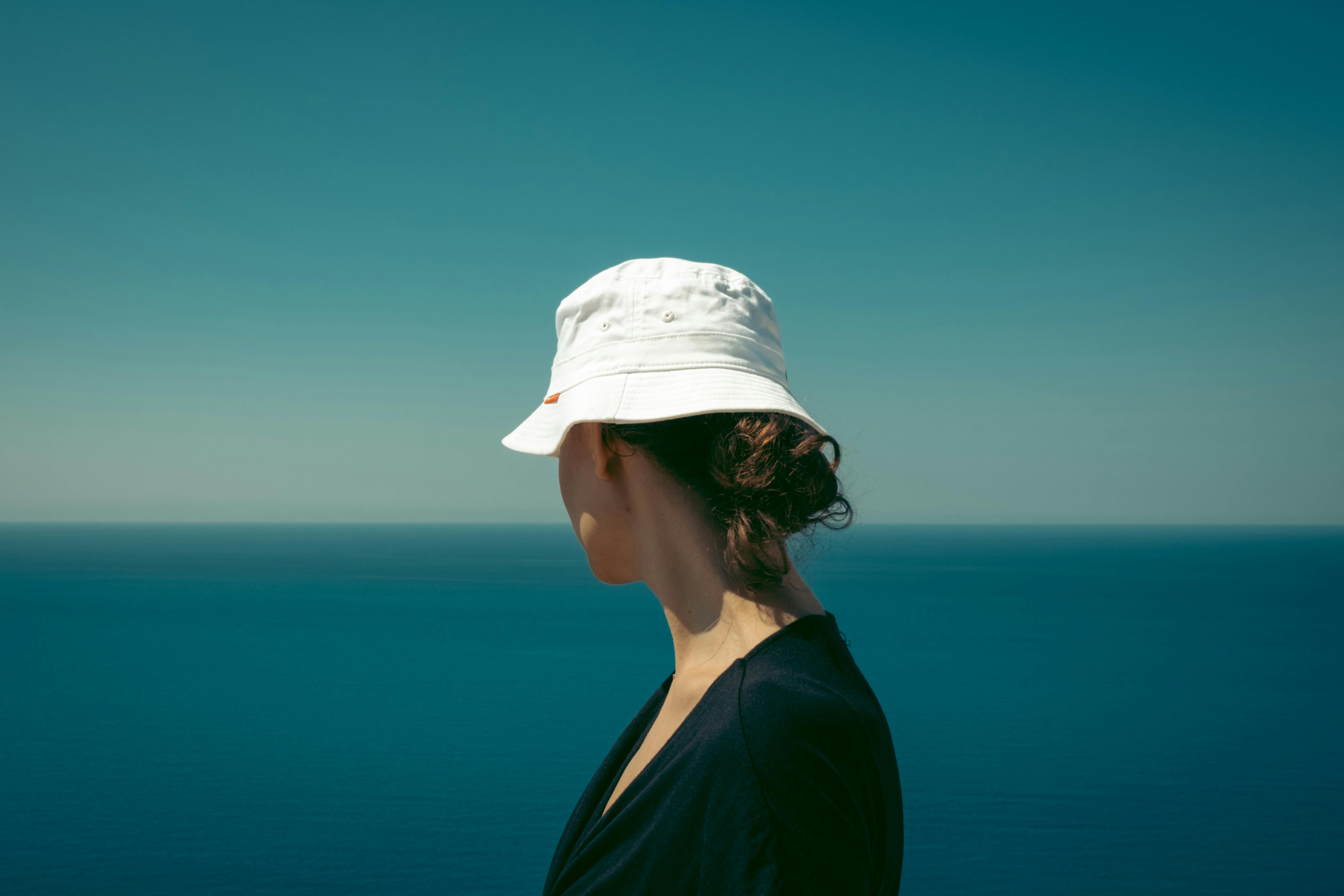 A serene view of a woman in a hat gazing over the ocean in Lefkada, Greece, under a clear blue sky.