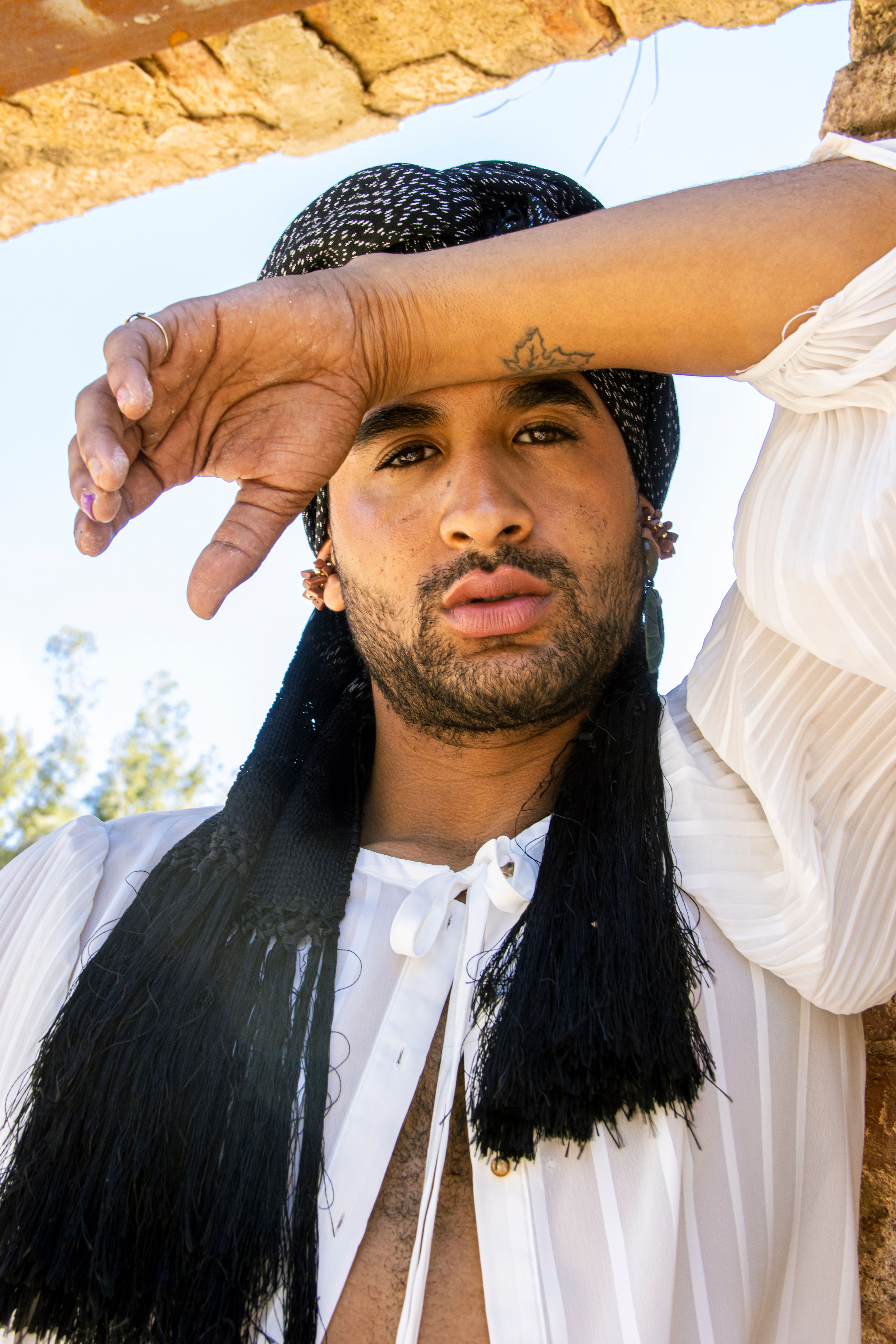 Fashionable portrait of a man in a black headwrap posing outdoors with a stylish expression.