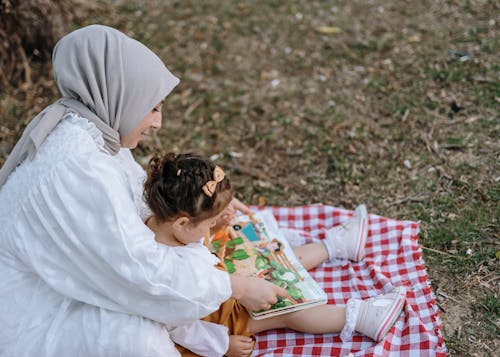 A woman and child reading a book on a picnic blanket