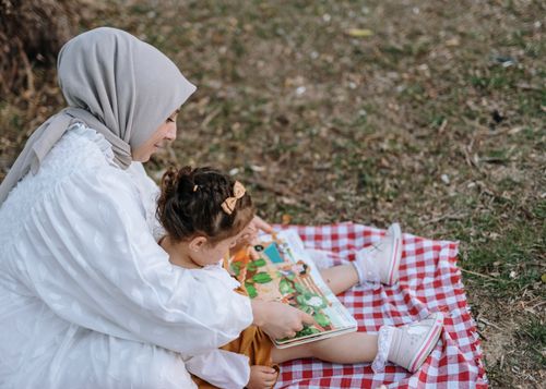 Free Mother and daughter enjoying a book on a picnic blanket in a park setting. Stock Photo