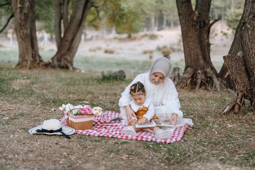A woman and child are sitting on a picnic blanket