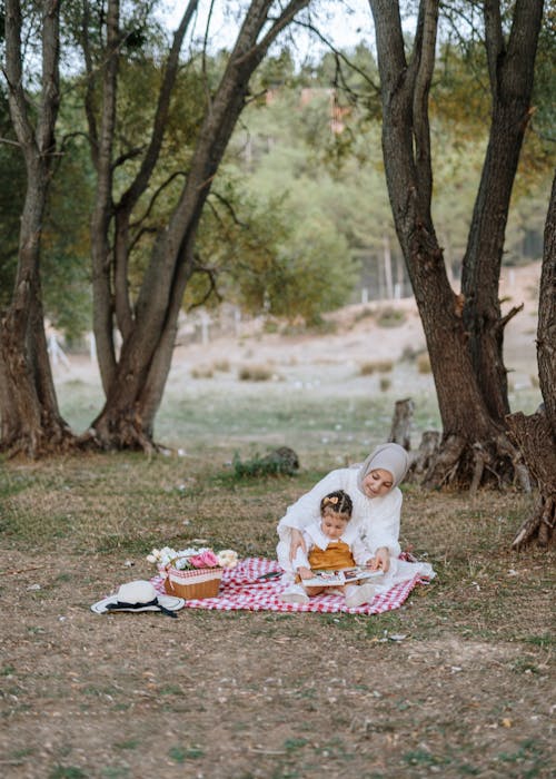 A woman and child are sitting on a blanket in the woods