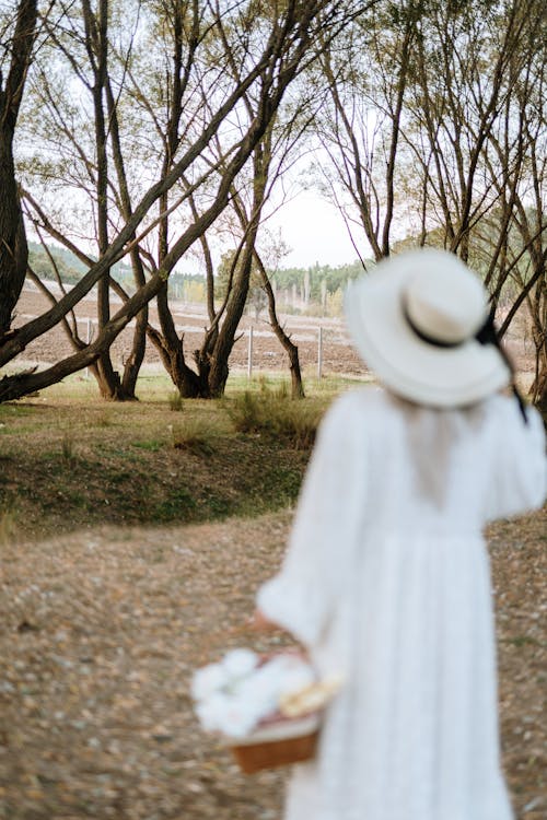 A woman in a white dress and hat walks through the woods