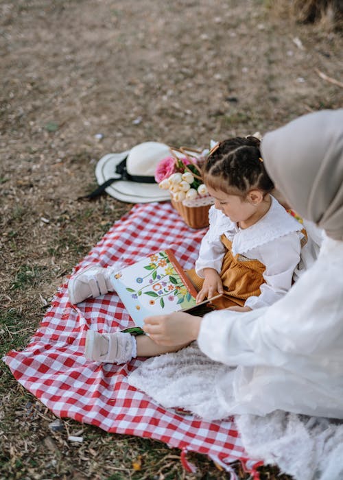 A woman and a child sitting on a picnic blanket