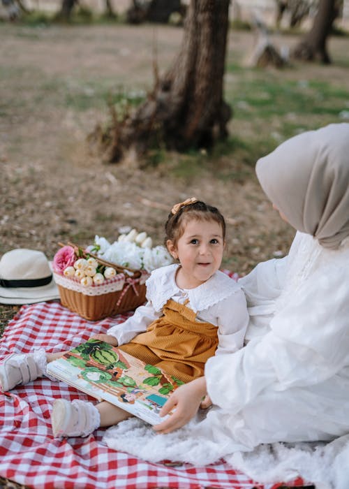 A woman and child sitting on a blanket in the park