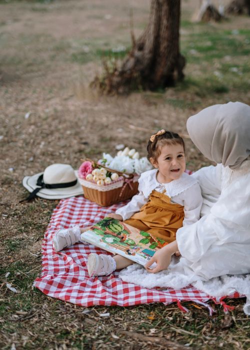 Free A serene outdoor picnic scene with a mother reading to her child on a checkered blanket. Stock Photo