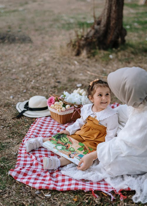 A woman and a child sitting on a blanket in the grass