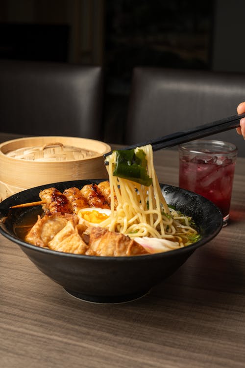 A person is holding chopsticks over a bowl of ramen