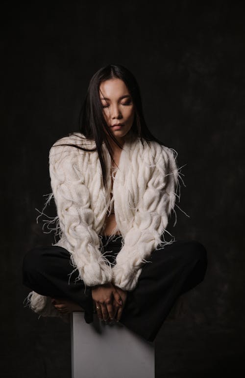 A woman sitting on a box wearing a white fur coat