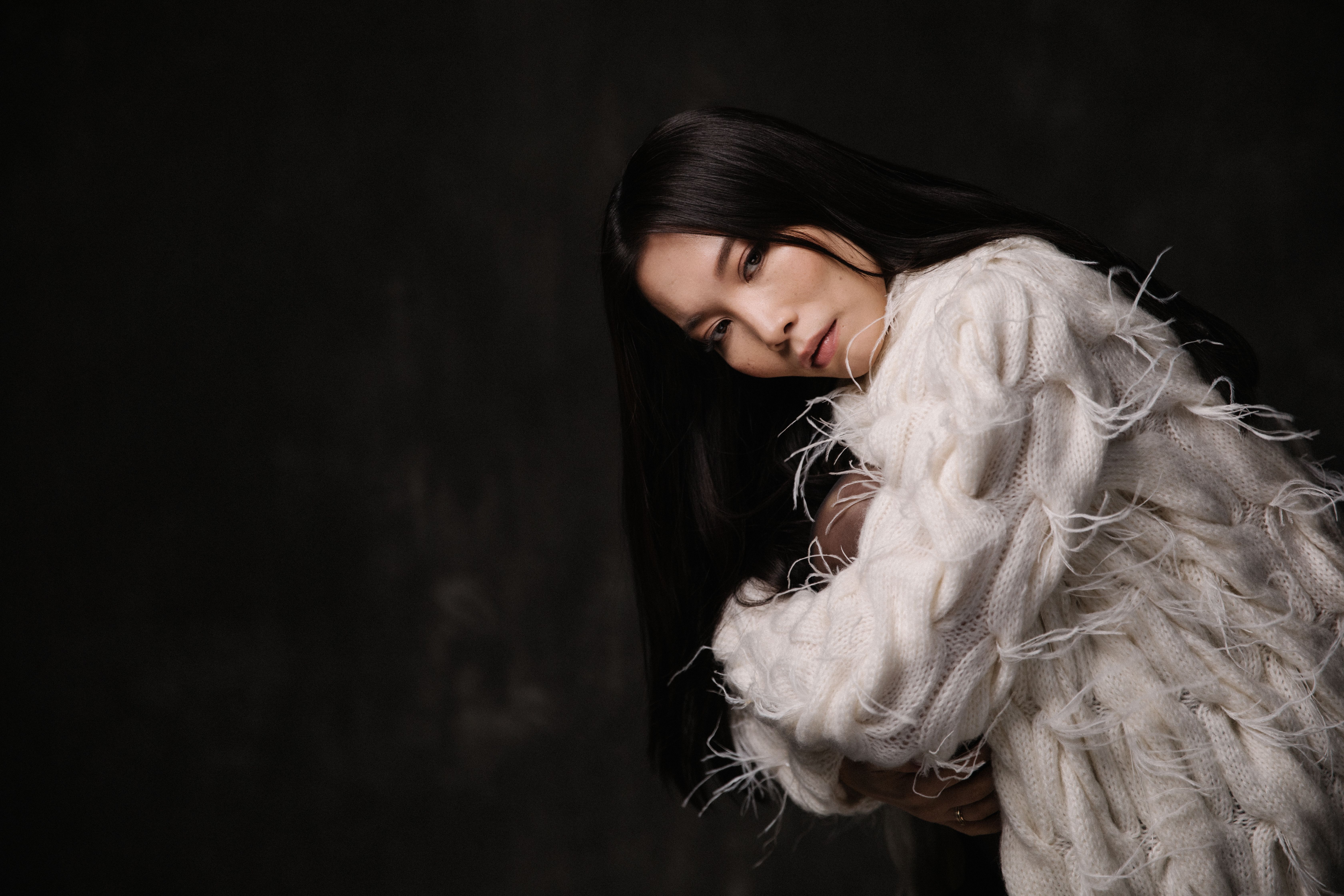 Stylish portrait of a woman wearing a textured white sweater in a dark setting.