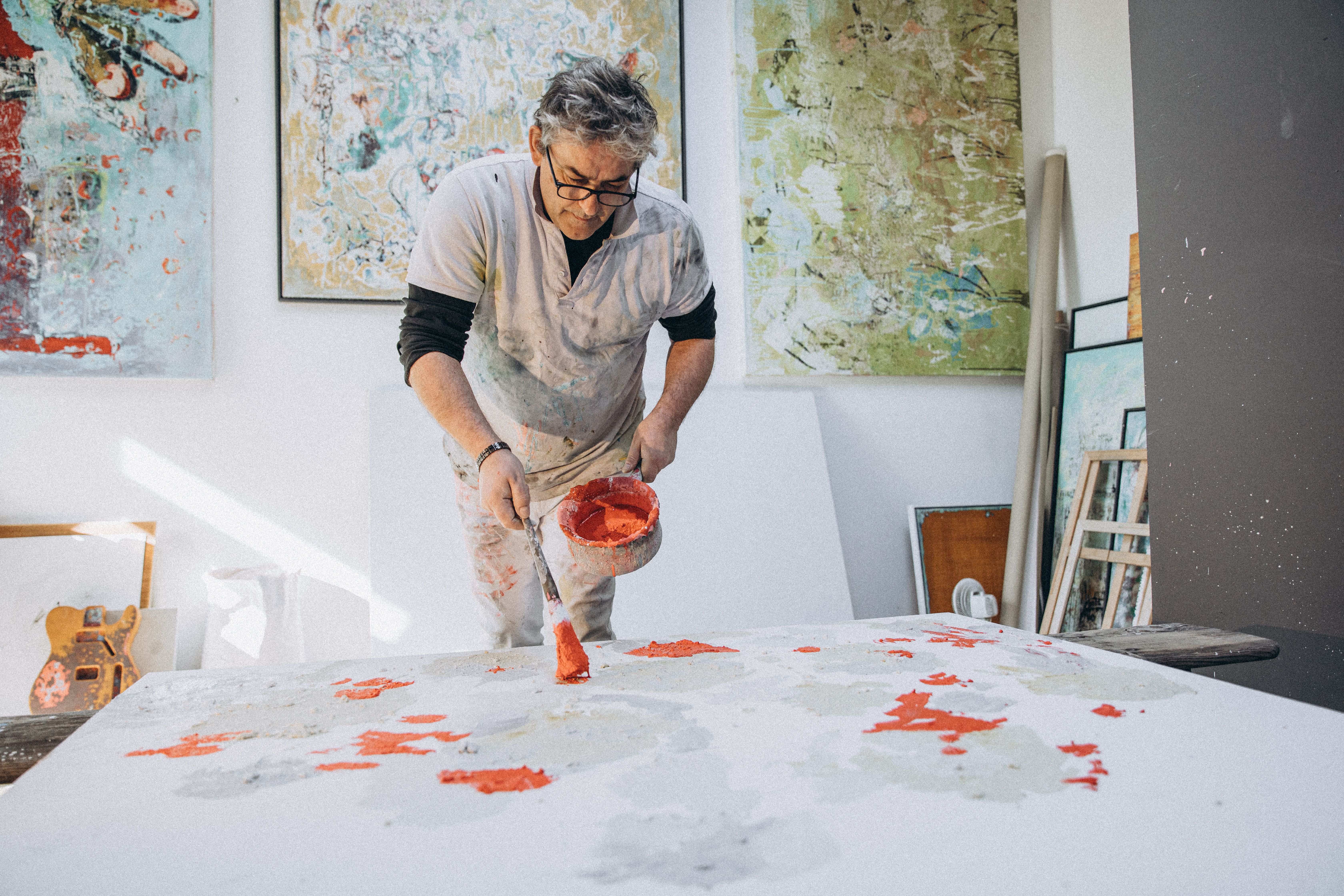 An artist in a studio applying vibrant colors on a canvas, creating abstract art.
