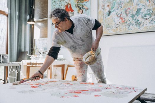 A senior male artist creating vibrant artwork in a well-lit studio with large windows.